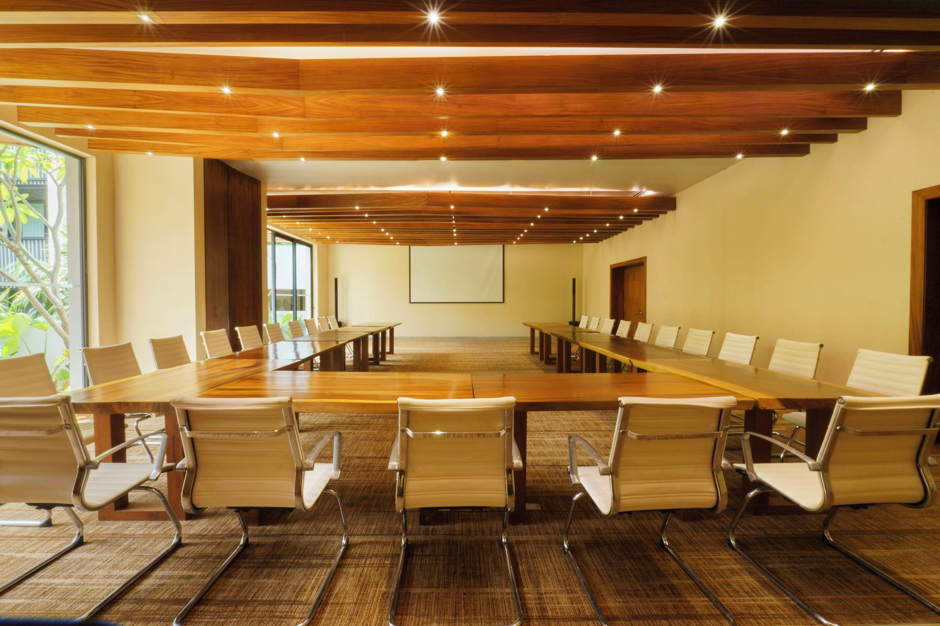A conference room with a long table, chairs, and a projector screen.