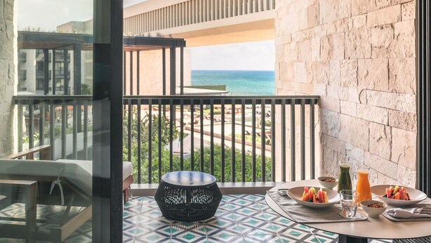 A balcony with a view of the ocean, a dining table with breakfast, and a decorative bowl.