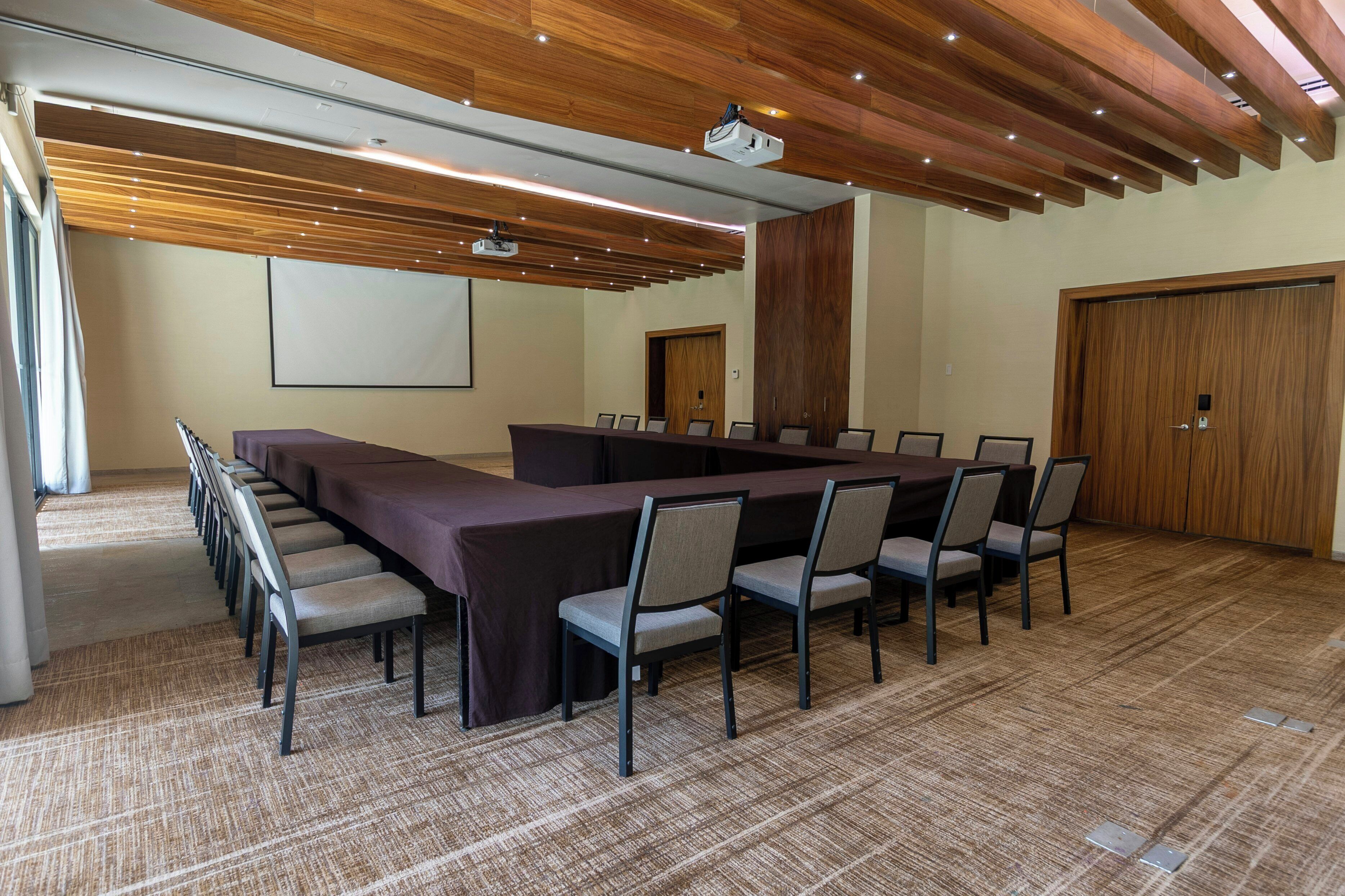 A conference room with a long table, chairs, a projector, and a screen.