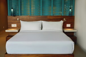 A modern hotel room with a wooden headboard, a large bed, bedside tables, and a wall-mounted light fixture.