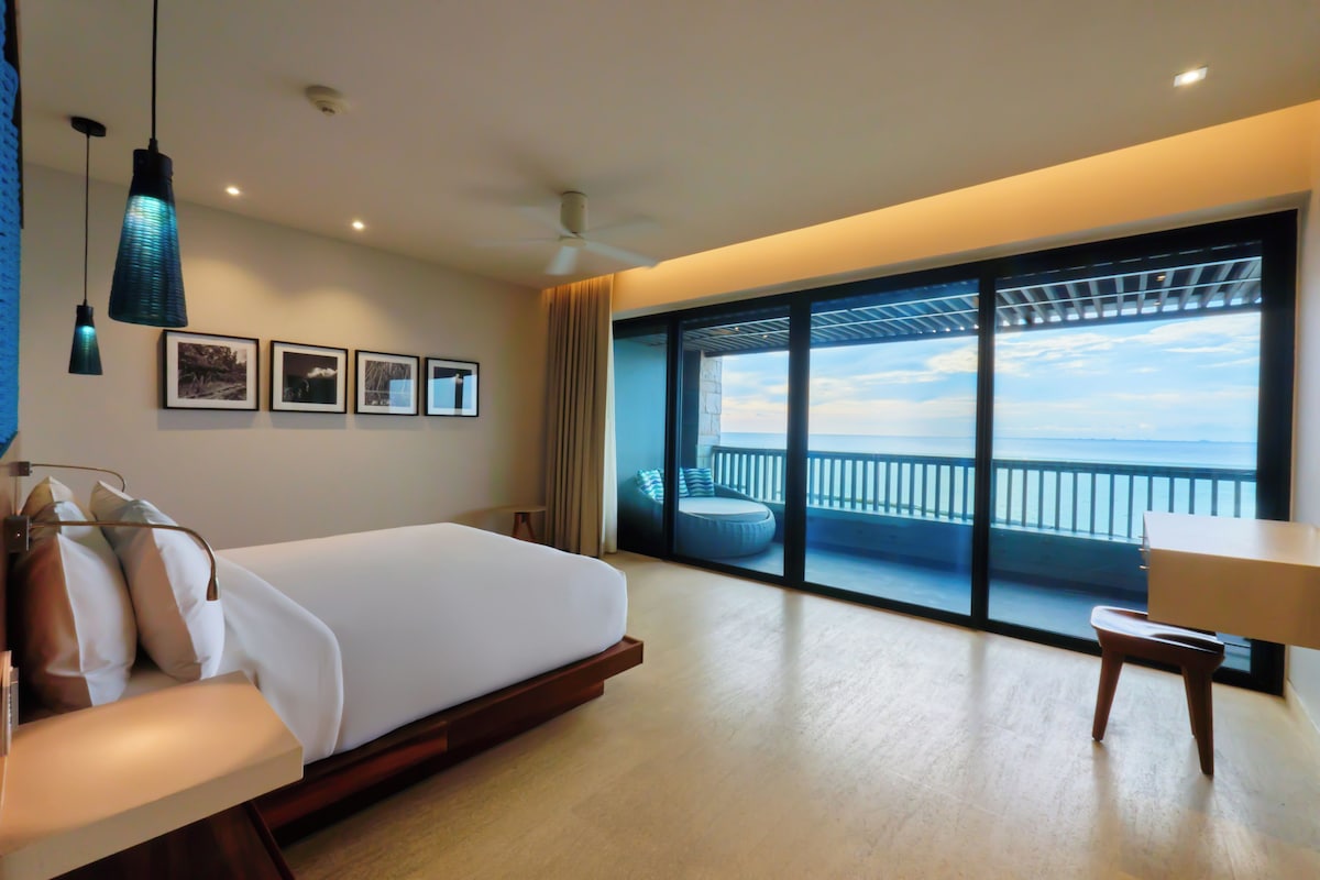 A modern hotel room with a large bed, a desk, and a balcony with a view.