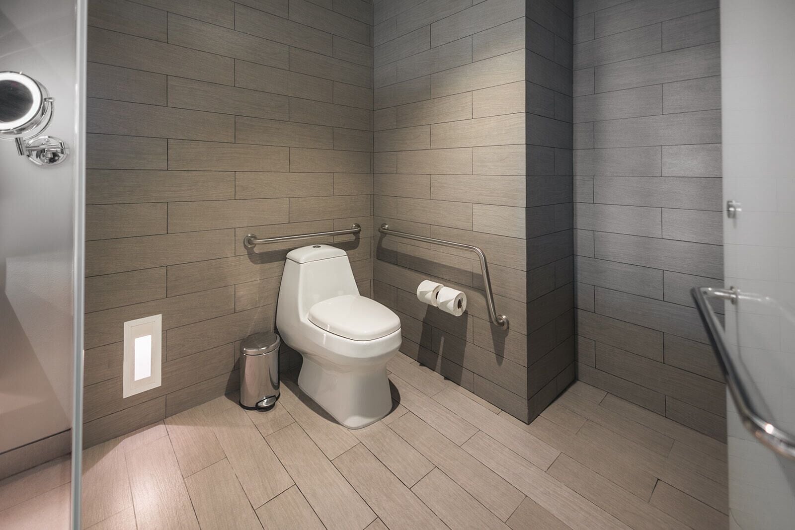 Un baño moderno con inodoro, barras de apoyo y un cubo de basura.