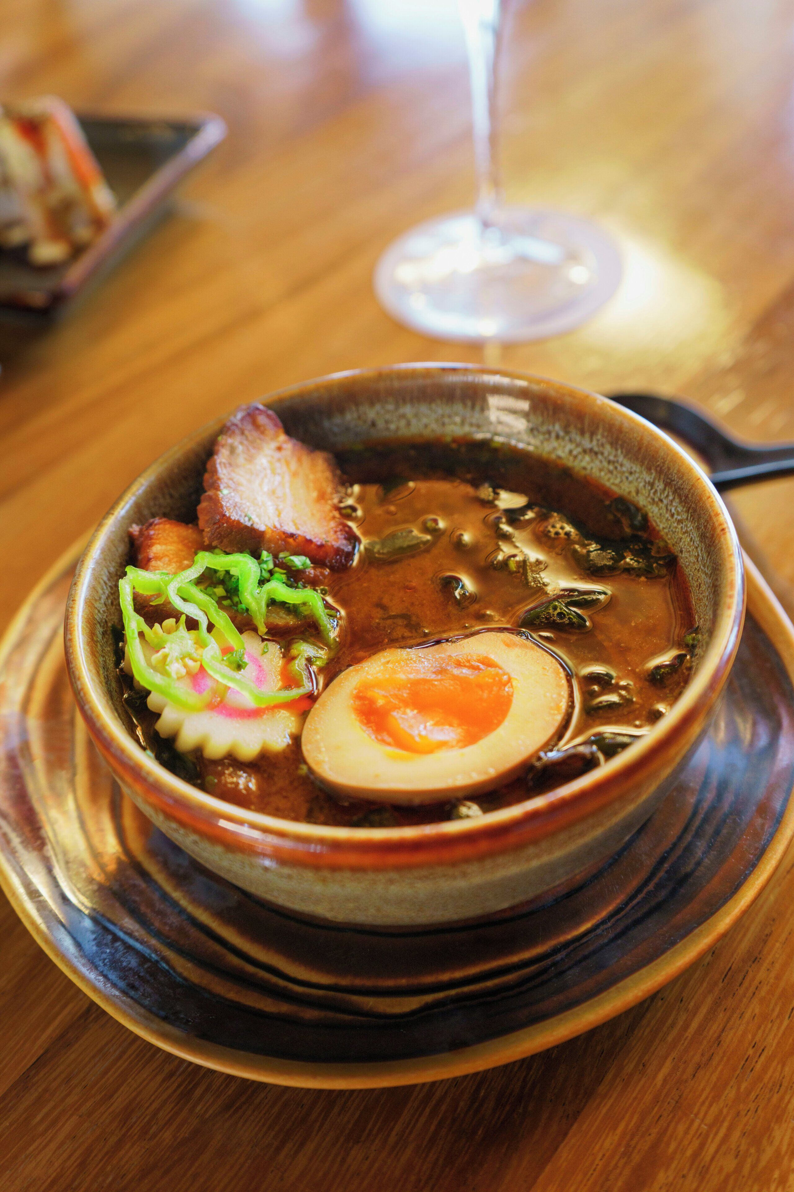 A bowl of soup with a poached egg, meat, and vegetables on a ceramic plate.