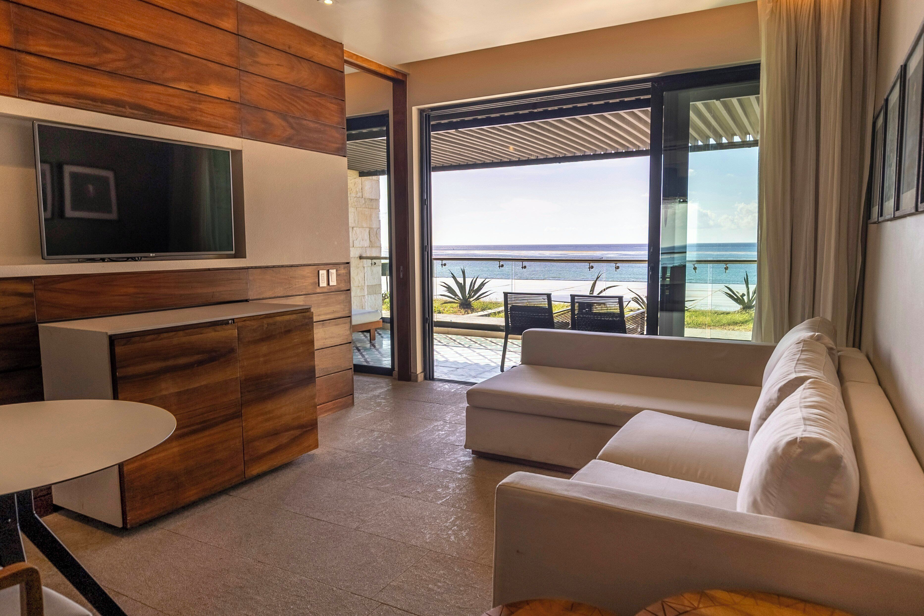 A modern living room with a flat-screen TV, wooden paneling, a sofa, and a view of the ocean.