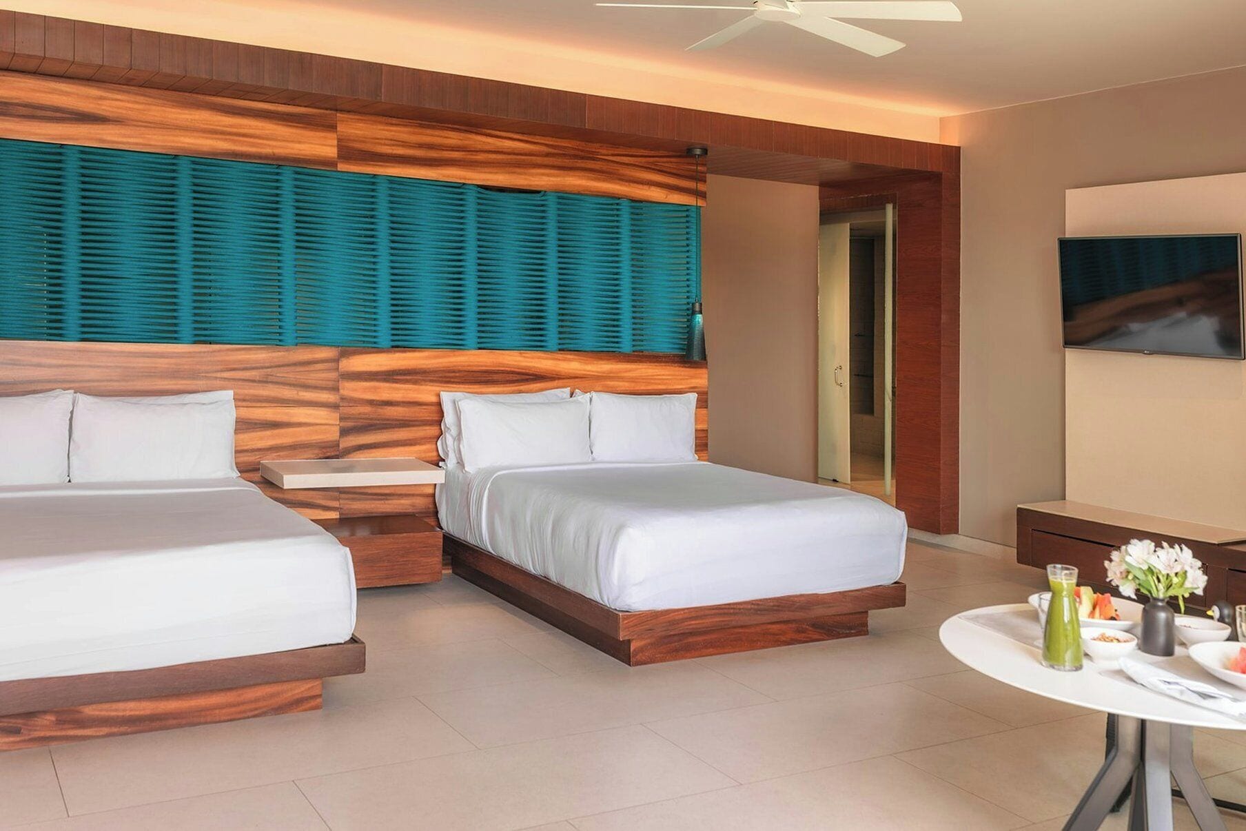 A hotel room with two beds, a small table with a drink and flowers, and a TV.