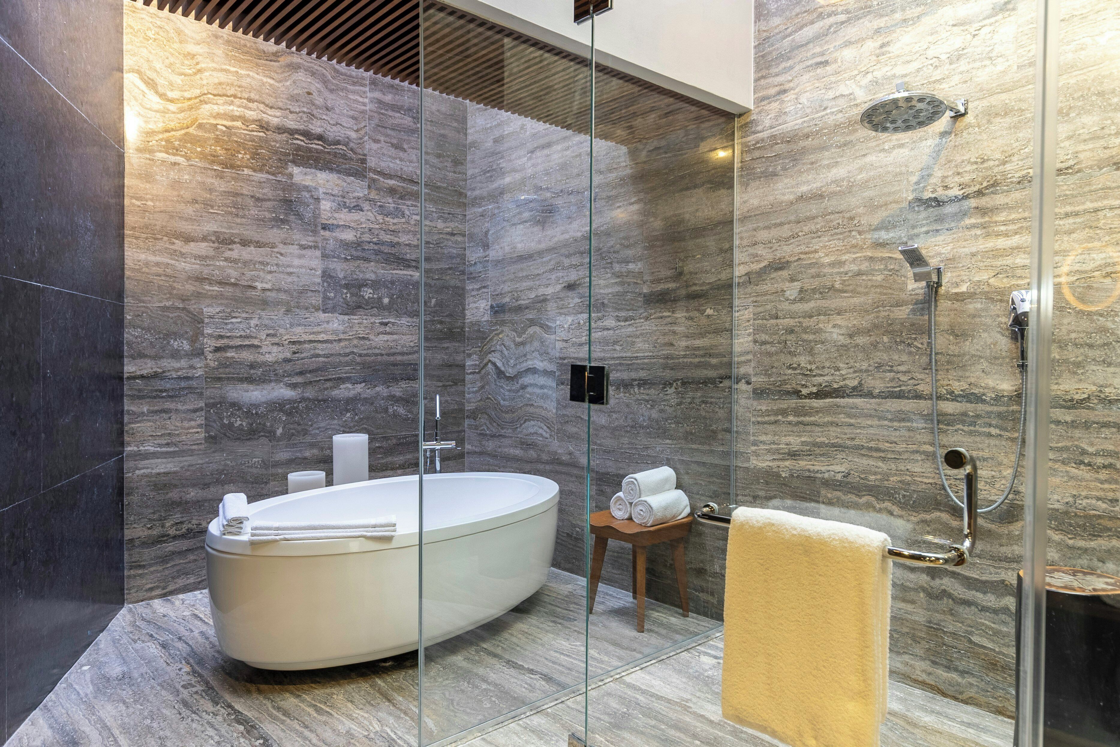 Un baño moderno con una bañera independiente, cabina de ducha de vidrio y paredes de mármol.