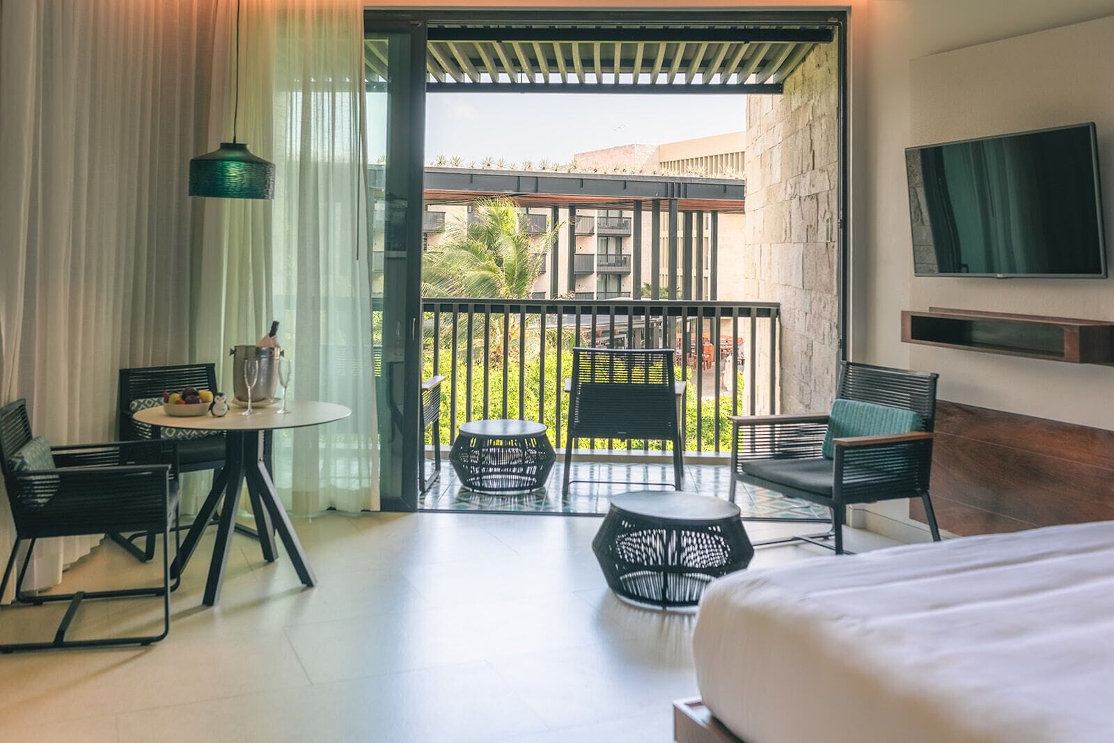 A hotel room with a balcony, a bed, a TV, and a dining area with chairs and a table.