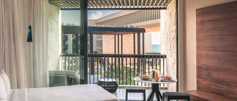 A hotel room with two beds, a balcony with a table and chairs, and a view of the sea.