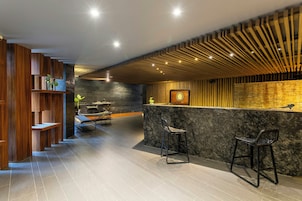 Un moderno área de recepción de spa con un mostrador de madera, dos taburetes y una pared de piedra.