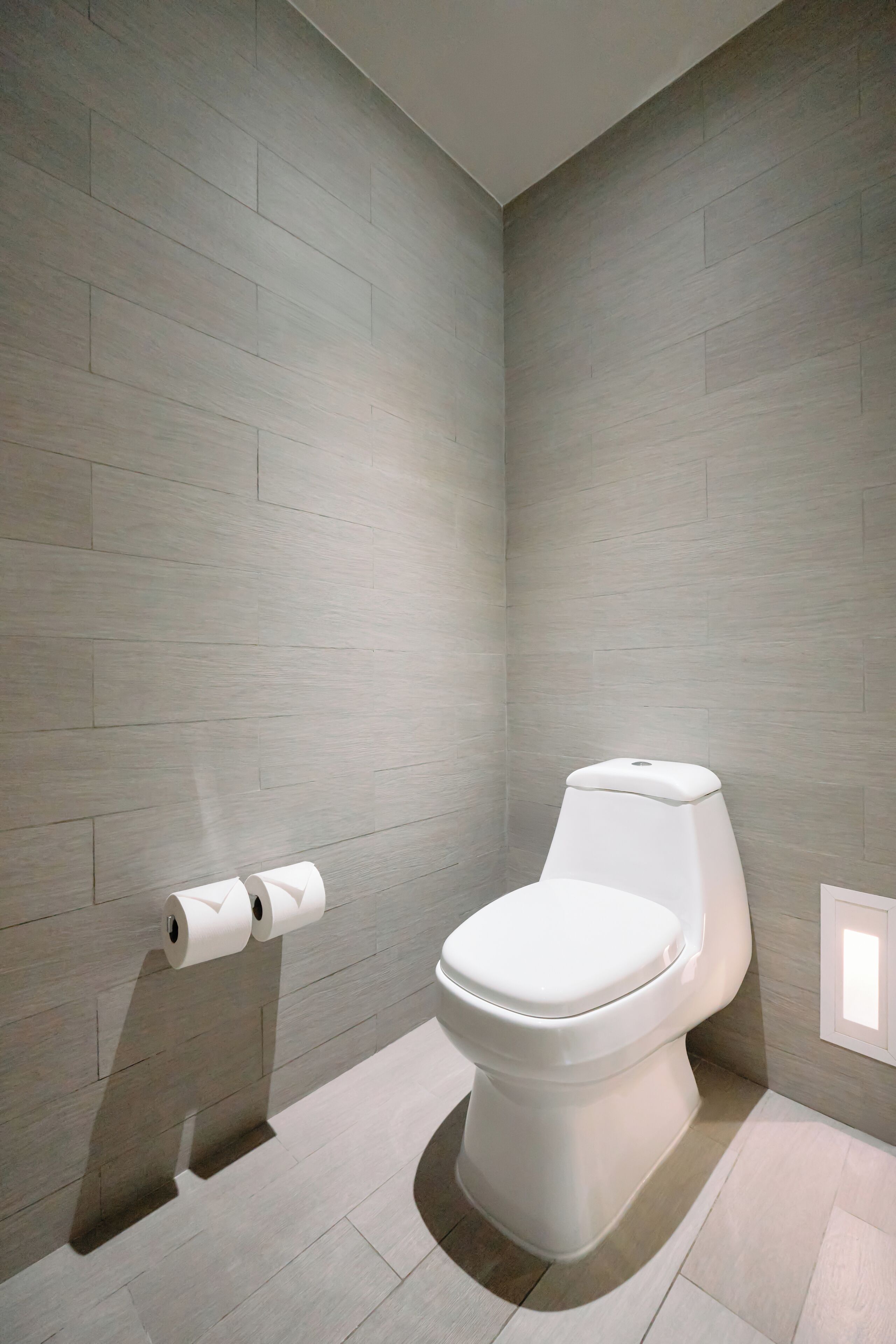 A modern bathroom with a toilet, a toilet paper holder, and a light switch on the wall.