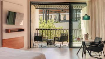 Une chambre d’hôtel avec un lit, un balcon avec des chaises, une table avec une bouteille et des verres, et un luminaire suspendu.