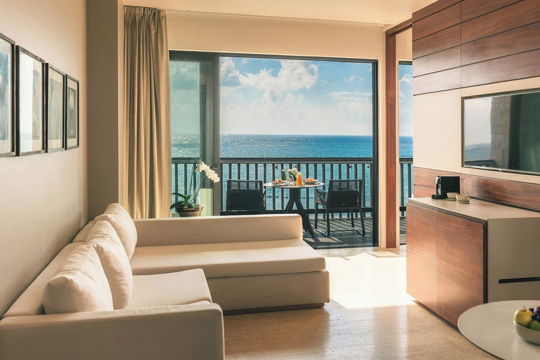 Una habitación de hotel moderna con balcón, sofá, mesa de comedor y televisor.