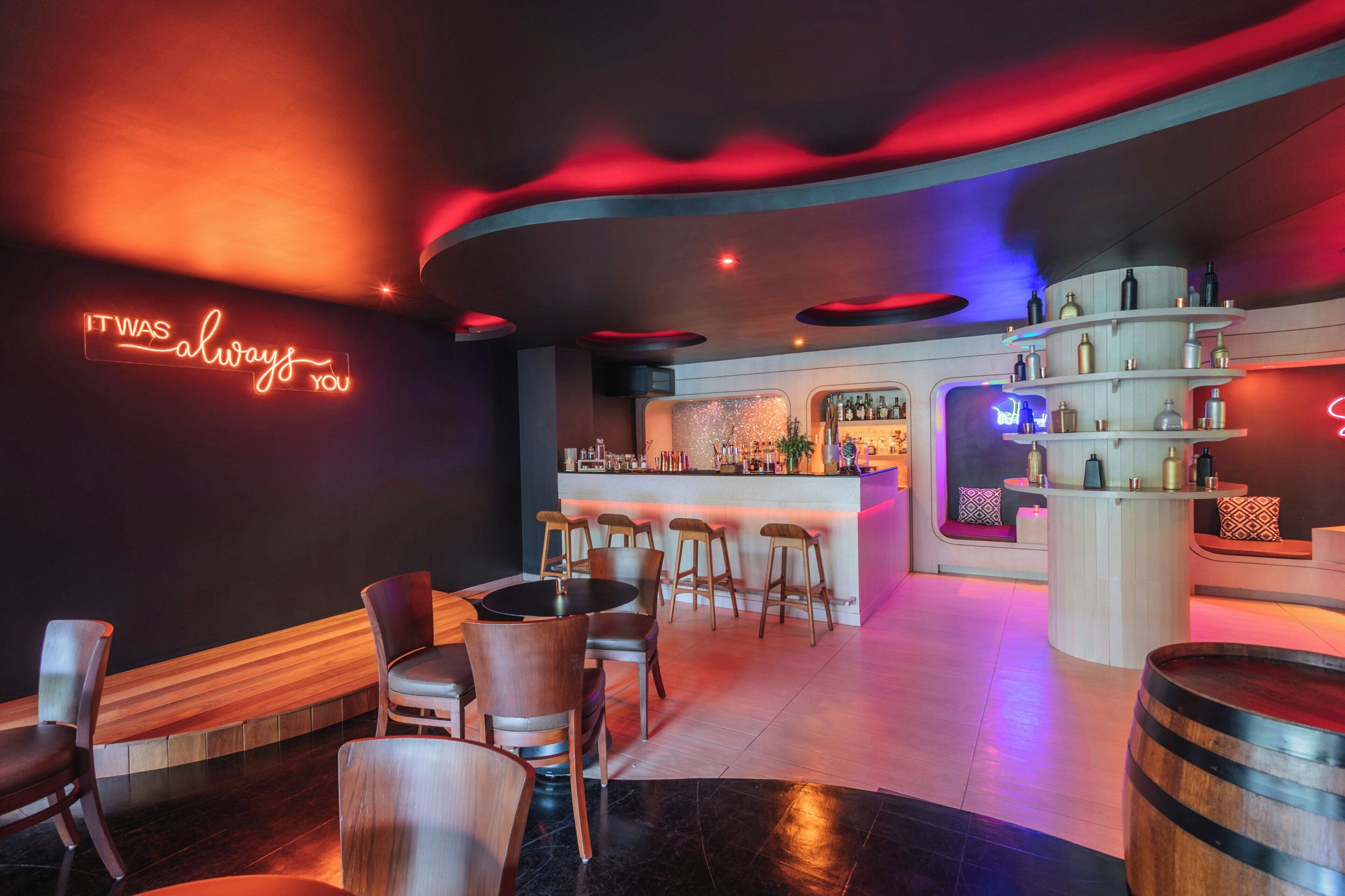 A bar area with a neon sign, wooden furniture, and a bar counter.