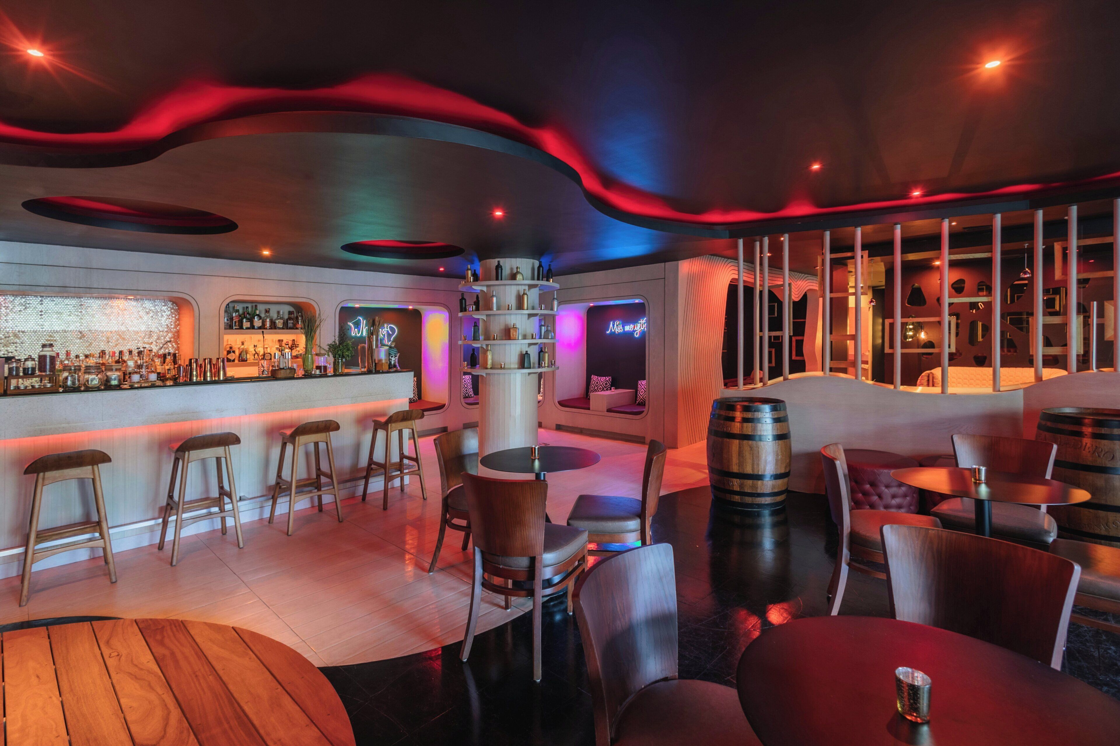 A bar area with stools, a bar counter, and shelves with bottles.