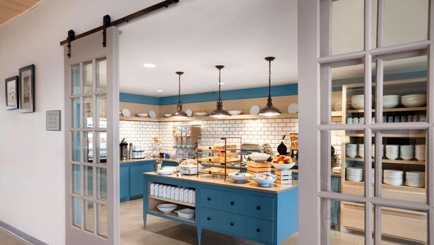 A kitchen with a blue island, white cabinets, and hanging pendant lights. - Country Inn & Suites by Radisson, Enid, OK (Enid)