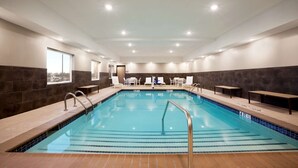 A large indoor swimming pool with a tiled edge, benches along the sides, and a clear view of the sky through the windows. - Country Inn & Suites by Radisson, Enid, OK (Enid)