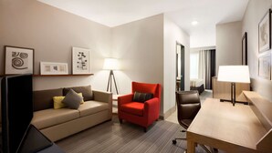 A hotel room with a sofa, a red armchair, a desk, a lamp, and framed artwork on the wall. - Country Inn & Suites by Radisson, Enid, OK (Enid)