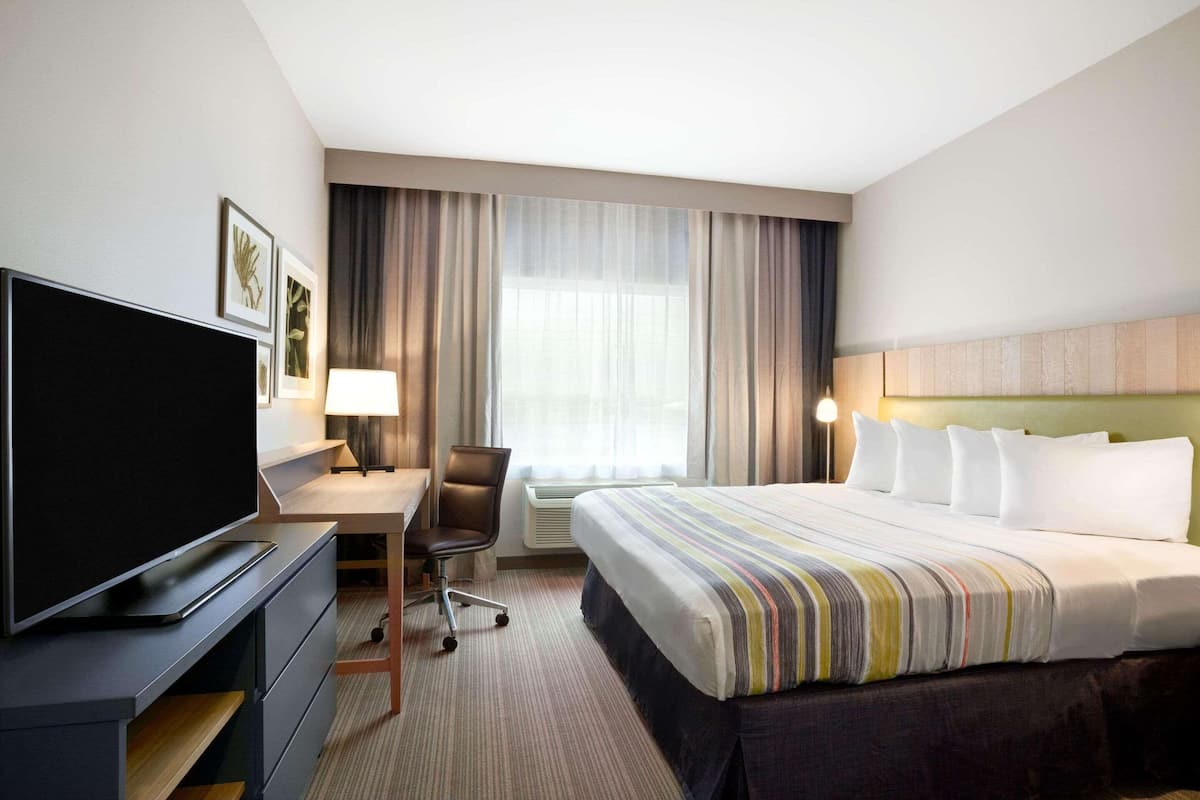A hotel room with a bed, a desk with a chair, a television, and a window with curtains.