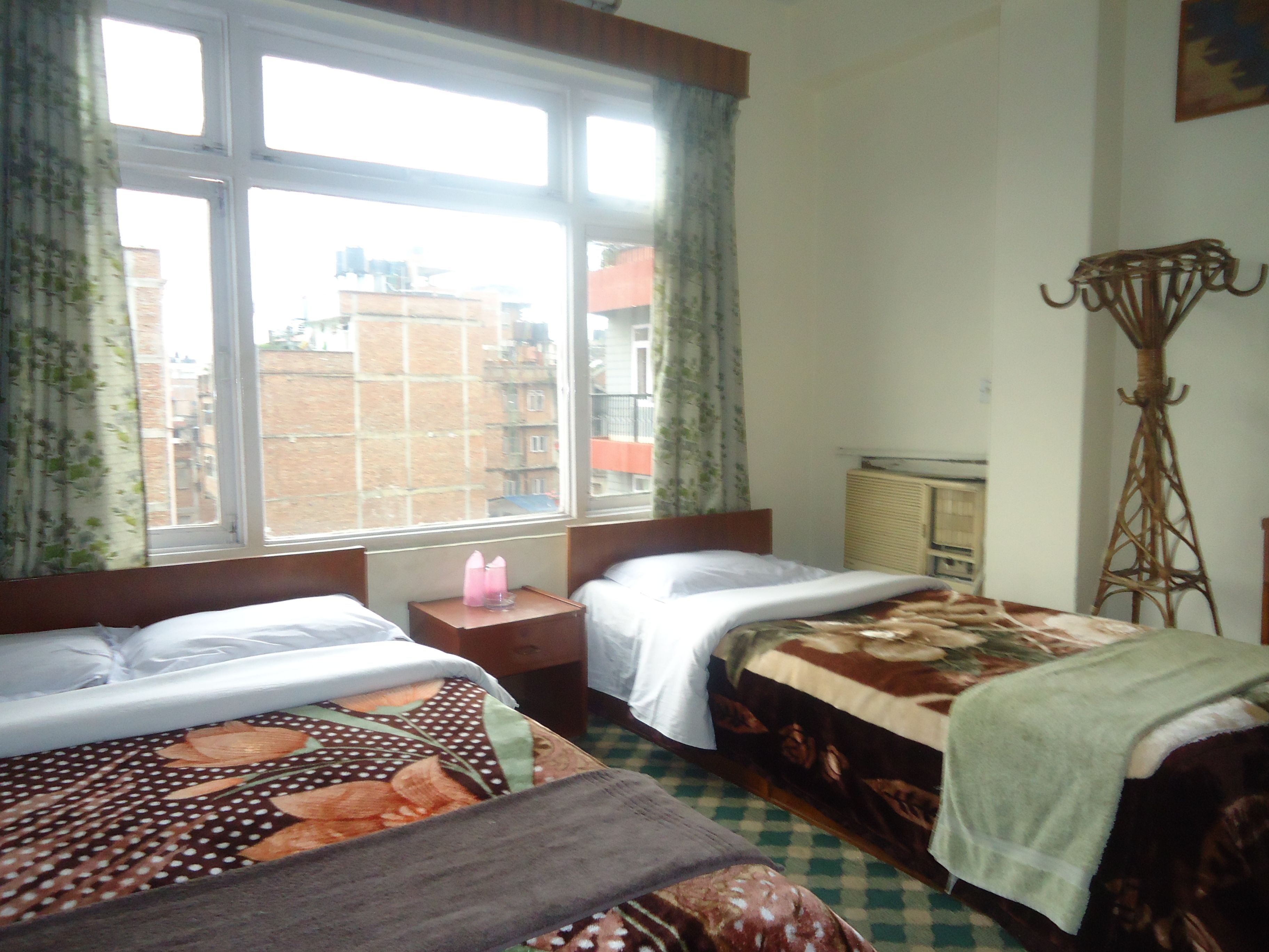 A hotel room with two beds, a window with curtains, a radiator, and a tall floor lamp.