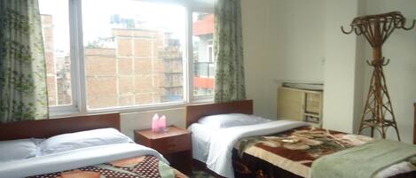 A hotel room with two beds, a window with curtains, a radiator, and a tall floor lamp.