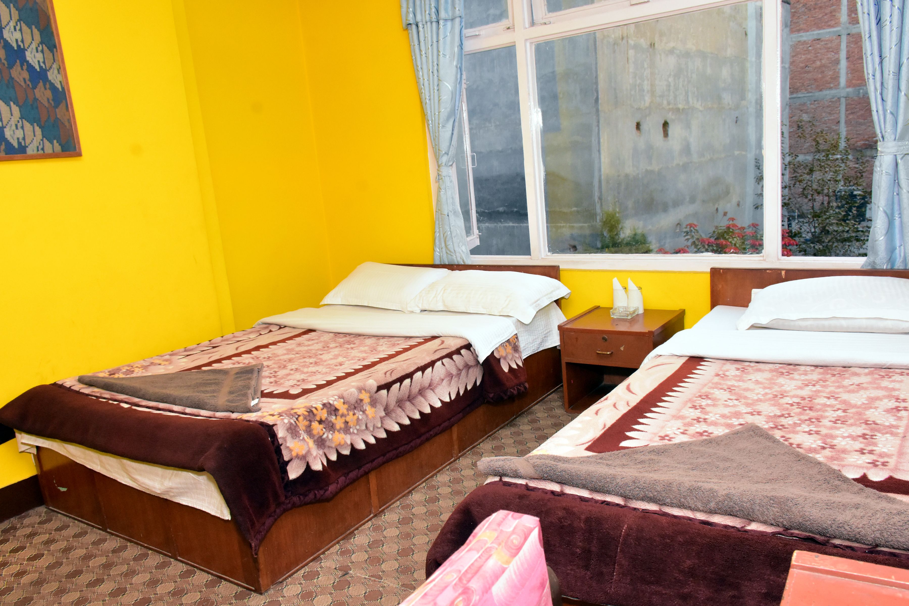 A room with two beds, a window with curtains, and a small bedside table with a lamp.