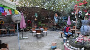 An outdoor seating area with tables and chairs, surrounded by plants and a brick wall. - Hotel Discovery Inn (Kathmandu)