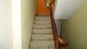 A staircase with a wooden handrail leading to a room with an orange wall and a door. - Hotel Discovery Inn (Kathmandu)
