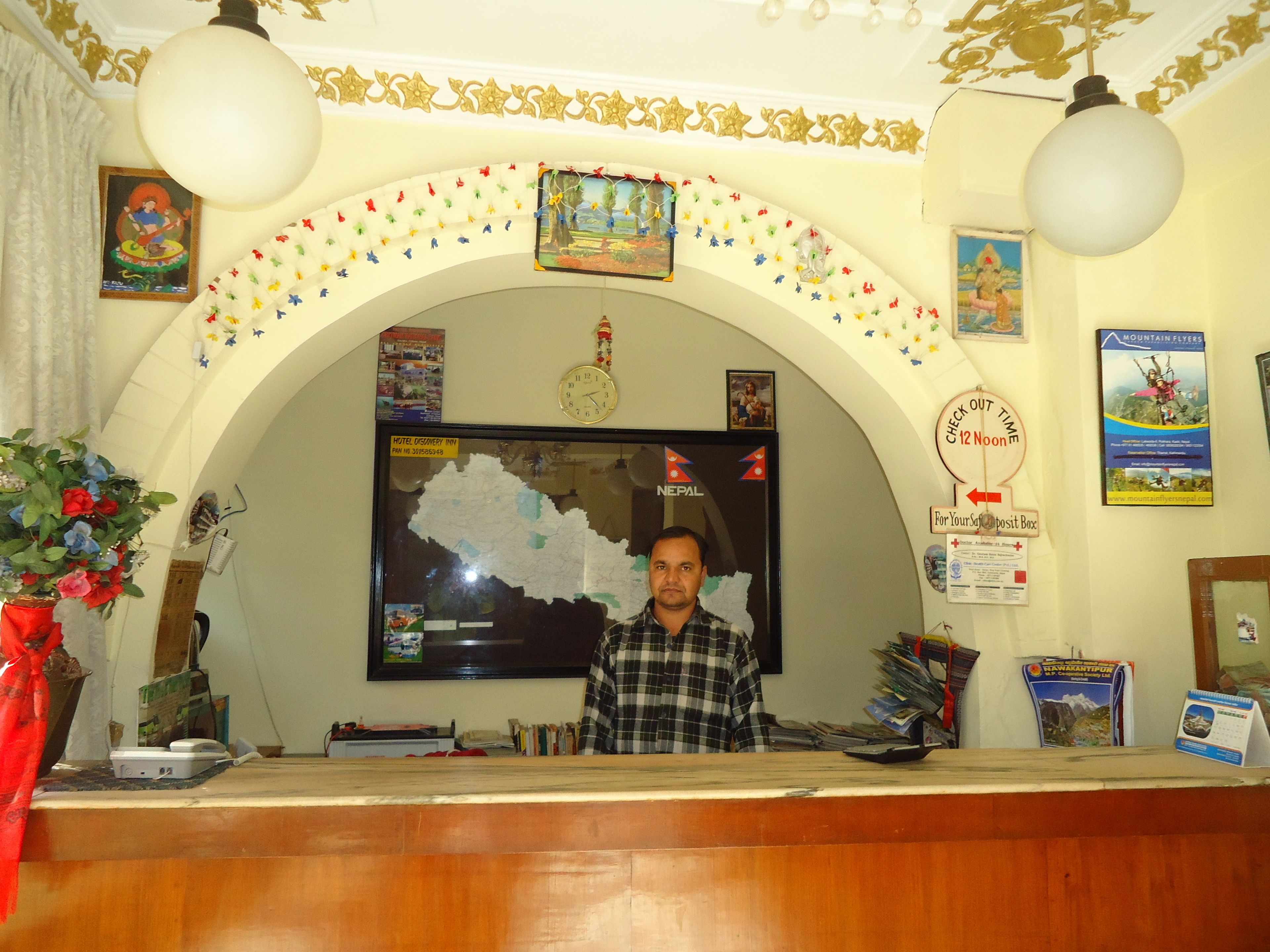 A reception desk with a map of Nepal, a clock, and various informational posters.
