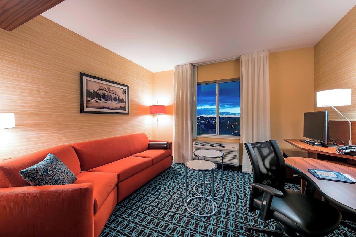 A hotel room with a red sofa, a desk with a computer, and a view of the city at night.