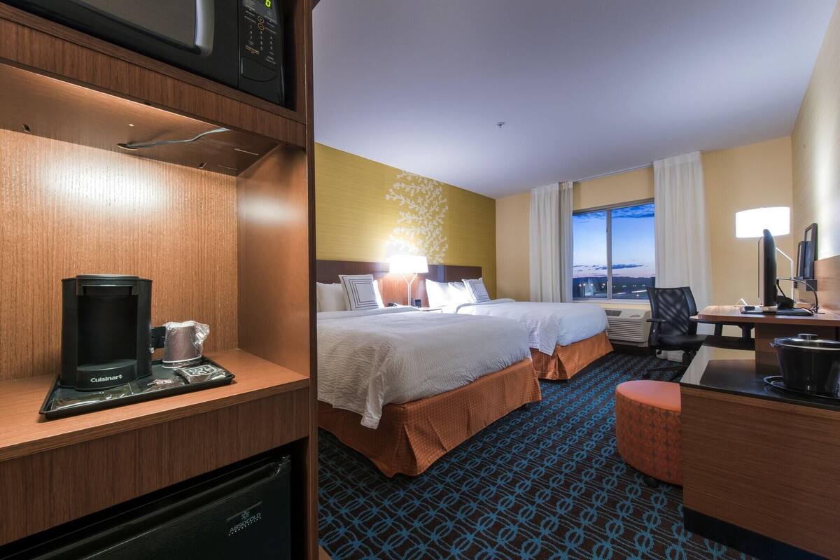 A hotel room with a bed, a desk, a minibar, and a view of the cityscape.