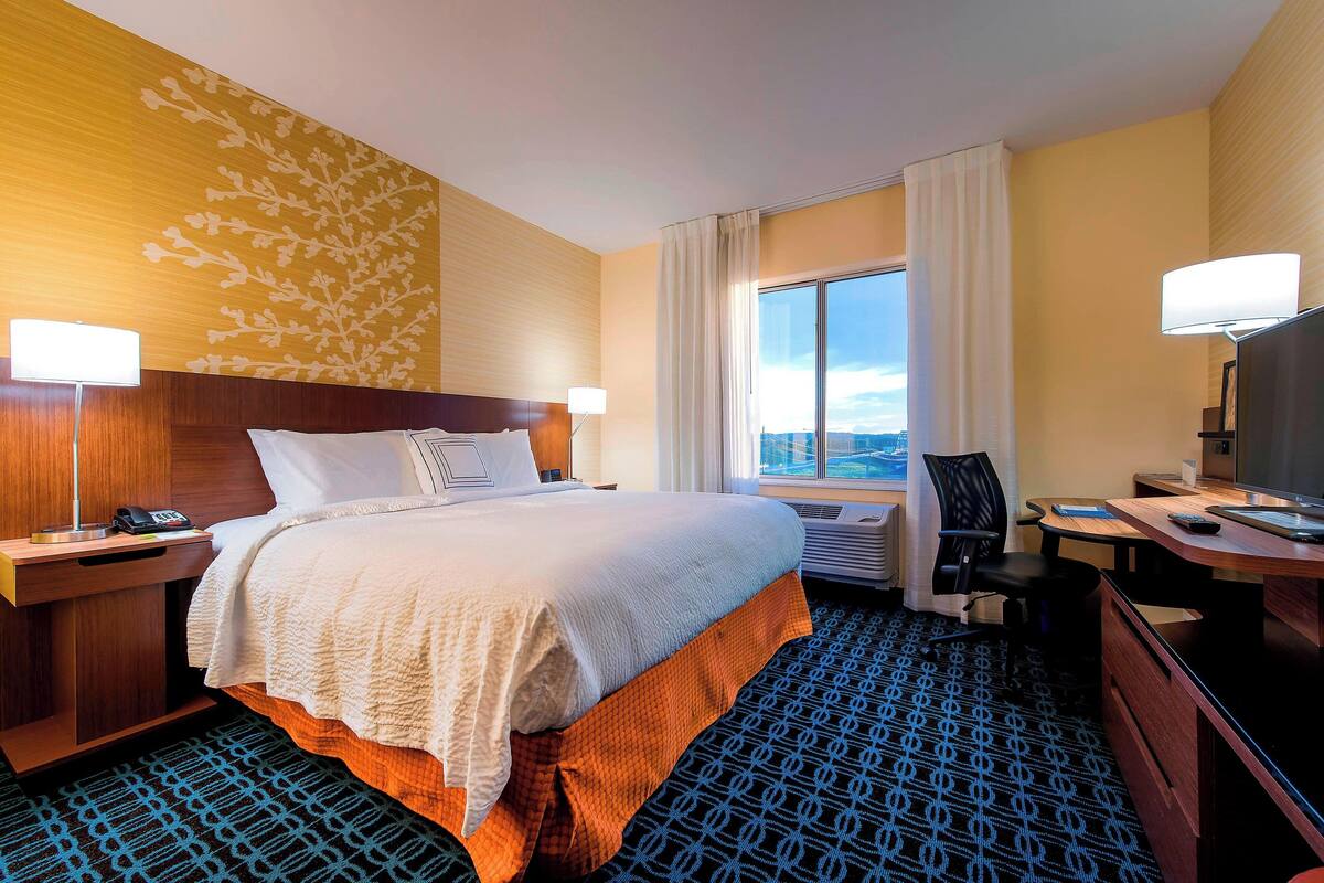 A hotel room with a large bed, a desk, a chair, and a view of the city.