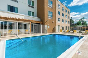 A swimming pool with a white fence, sun loungers, and a building with multiple windows.