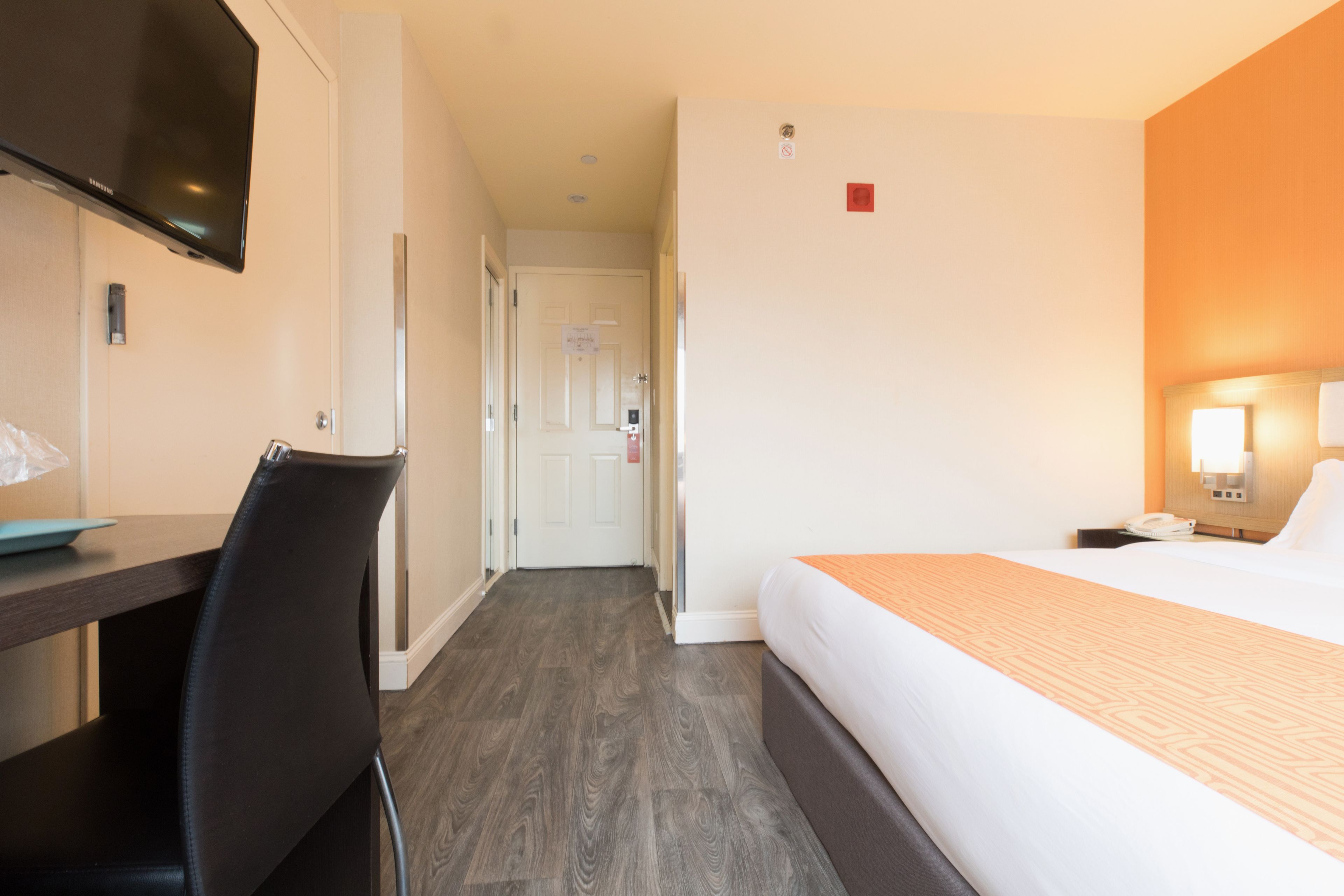 Une chambre d’hôtel avec un lit, un bureau, une chaise, une télévision et une porte.