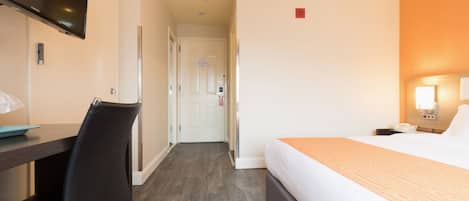 Une chambre d’hôtel avec un lit, un bureau, une chaise, une télévision et une porte.