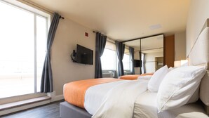 A hotel room with a large bed, a flat-screen TV mounted on the wall, and a window with curtains. - Romana Hotel - NYC (Long Island City)