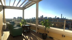A sunlit balcony with a city view, green seating, and potted plants. - Romana Hotel - NYC (Long Island City)