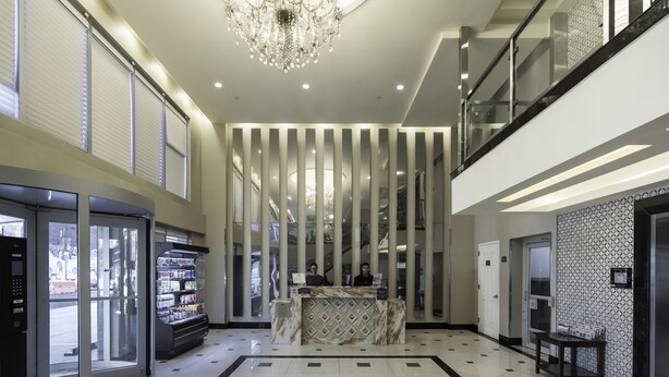 A hotel lobby with a reception desk, vending machines, a chandelier, and a patterned wall. - Romana Hotel - NYC (Long Island City)