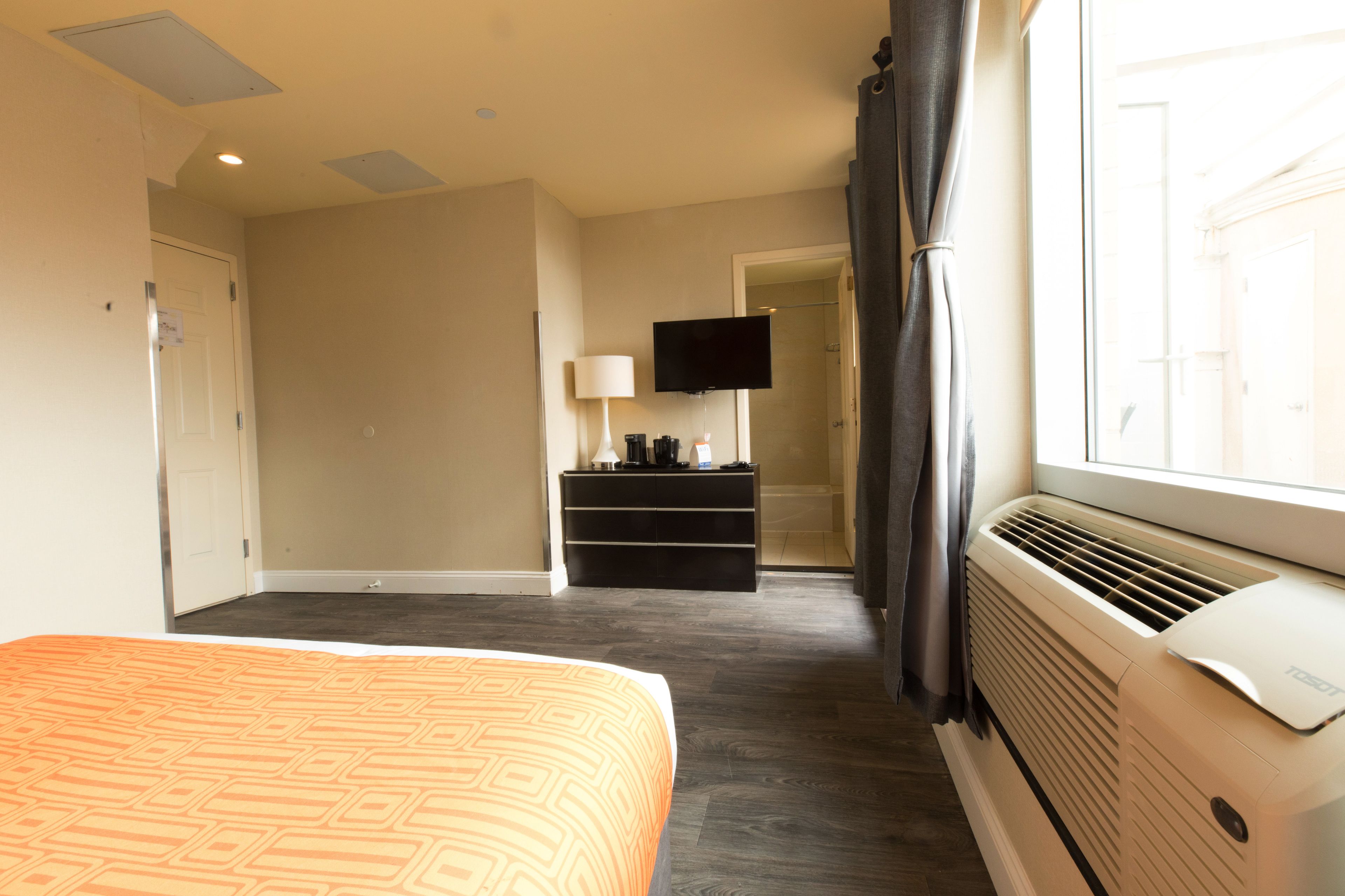 A hotel room with a bed, a TV, a heater, and a window with curtains.