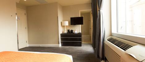 A hotel room with a bed, a TV, a heater, and a window with curtains.
