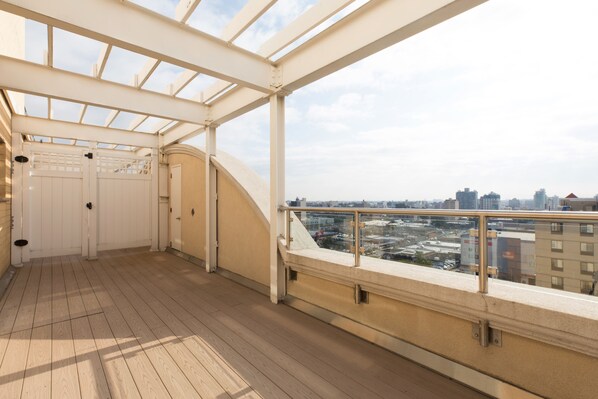 An empty balcony with a wooden floor and a glass railing, overlooking a cityscape. - Romana Hotel - NYC (Long Island City)