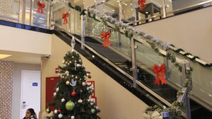 A multi-level shopping mall with an escalator decorated with red bows and tinsel. - Romana Hotel - NYC (Long Island City)