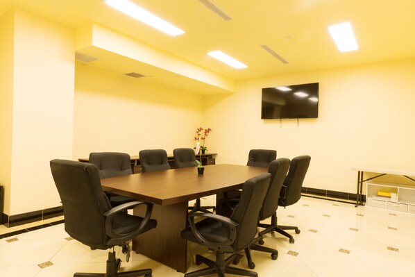 A conference room with a large table, six chairs, a TV on the wall, and a potted plant.