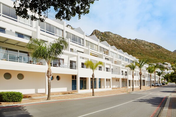 A modern hotel with a white facade, multiple balconies, and palm trees lining the street. - First Group Cape Gordonia (Cape Town)