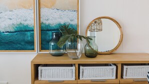 A wooden console with three white wicker baskets, two glass vases with plants, and a round mirror. - First Group Cape Gordonia (Cape Town)