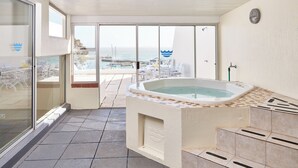 A balcony with a hot tub, glass doors leading to a pool area, and a view of the sea. - First Group Cape Gordonia (Cape Town)