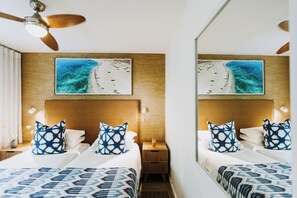 A hotel room with two beds, wooden headboards, a ceiling fan, and a large framed picture of a beach scene. - First Group Cape Gordonia (Cape Town)