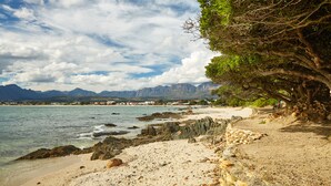 A coastal beach with rocky shoreline, clear water, and distant mountains. - First Group Cape Gordonia (Cape Town)