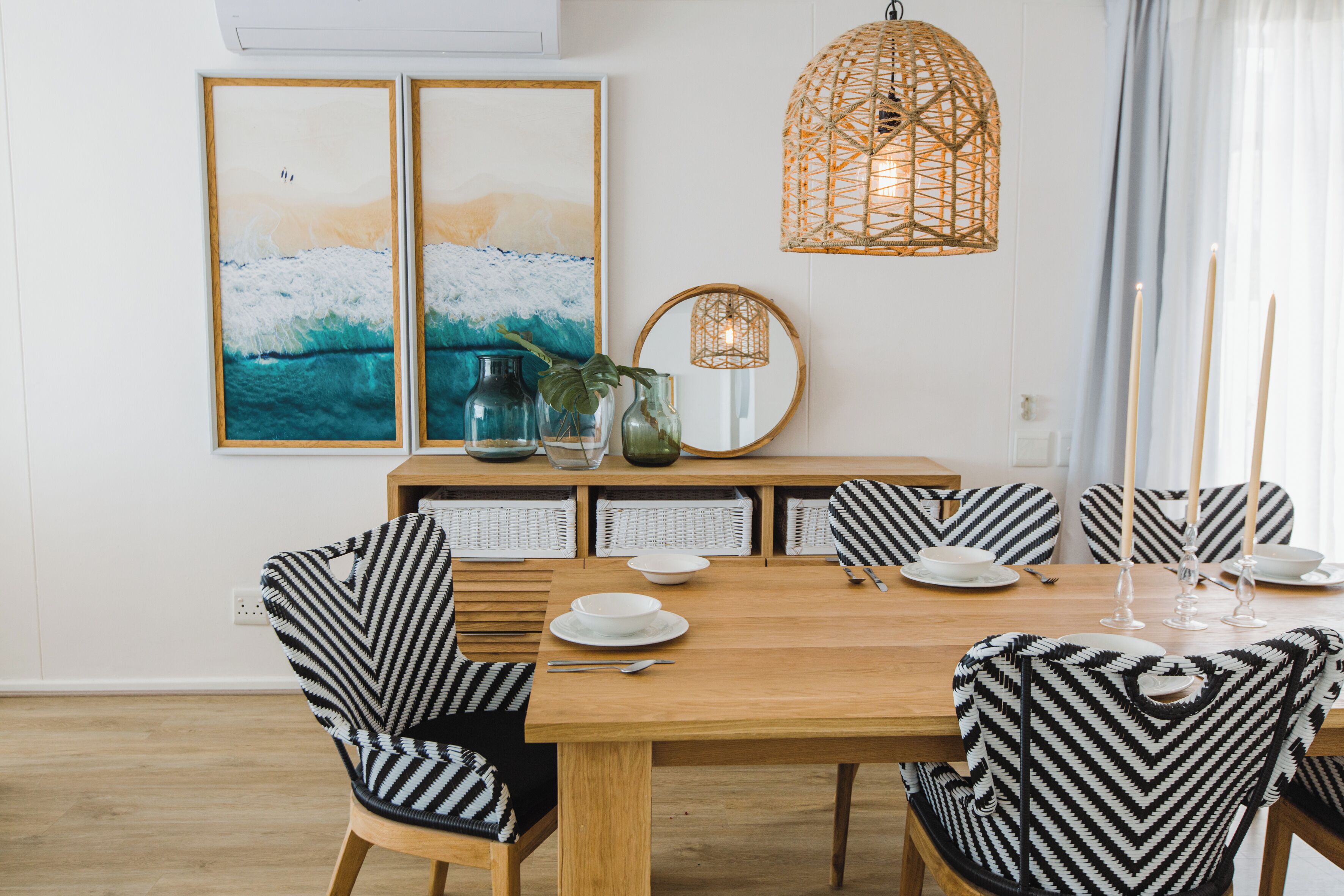 A dining area with a wooden table, black and white striped chairs, a woven pendant light, and framed artwork on the wall.