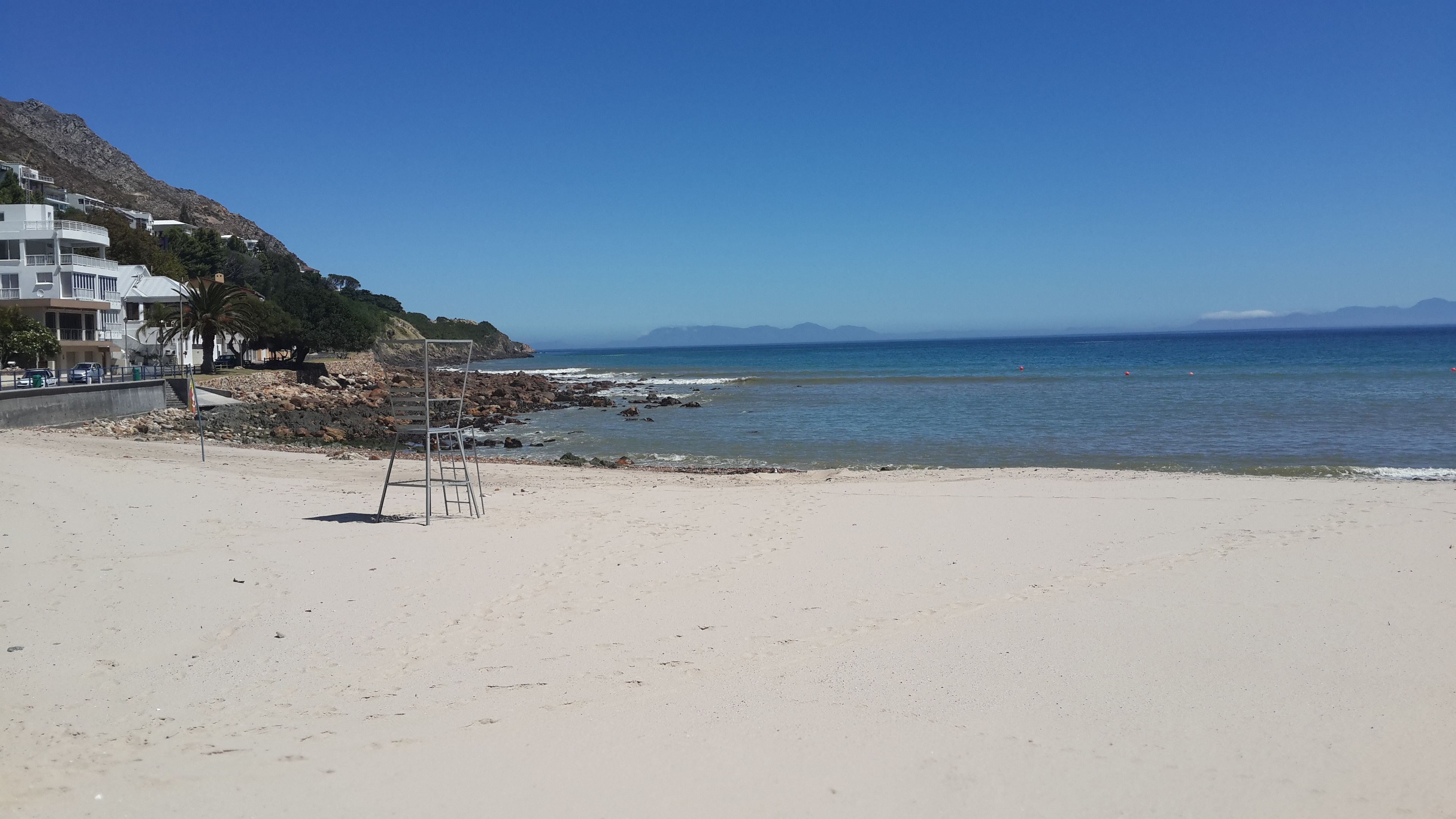 A beach with a metal chair and a rocky shoreline.