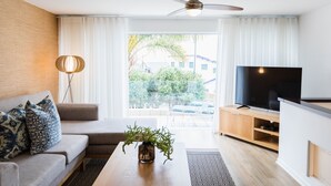 A modern living room with a sofa, a coffee table with a plant, a TV on a wooden stand, and a ceiling fan. - First Group Cape Gordonia (Cape Town)